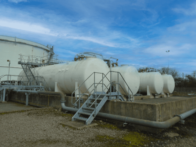 The image shows a large white machine at the Northampton fuel terminal. It is located outdoors under the sky with clouds in the background. The machine seems to be connected to pipes and storage tanks on the ground.
