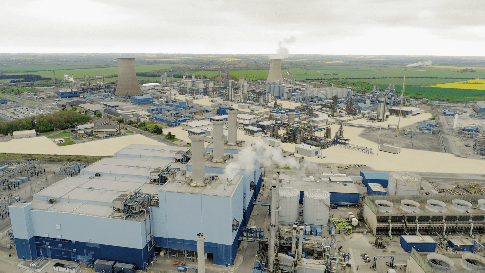 Aerial view of an industrial plant, sprawling complex, network of pipelines, large storage tanks, smokestacks emitting steam, overcast sky. Netherlands