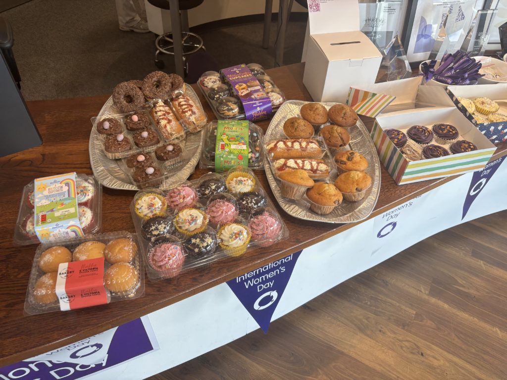 A table filled with a variety of cakes, muffins, and pastries at the px Stockton office bake sale for International Women’s Day, supporting women's empowerment.