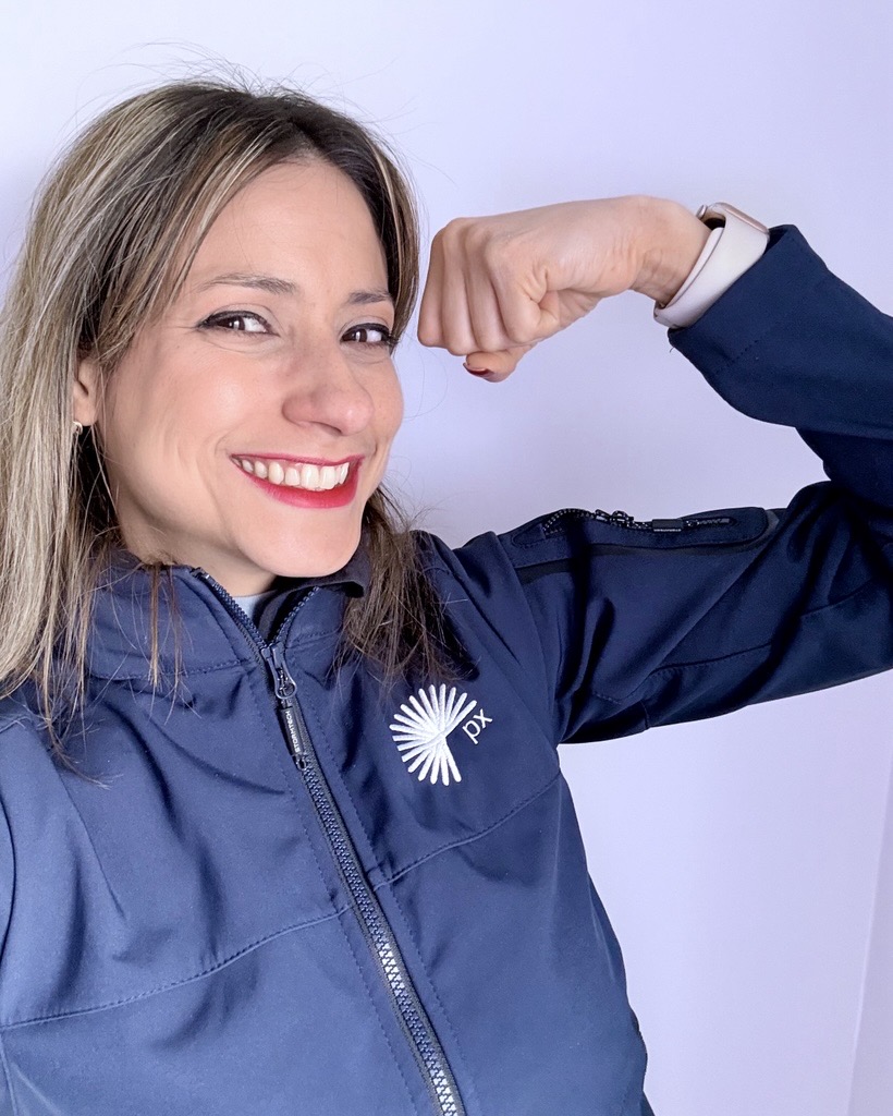 px female employee smiling and flexing her arm in a pose of strength representing the #AccelerateAction theme, celebrating women’s empowerment for International Women’s Day.